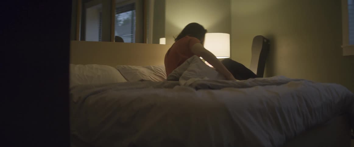 Woman with an orange shirt turns on the lamp and gets out of the bed in the bedroom