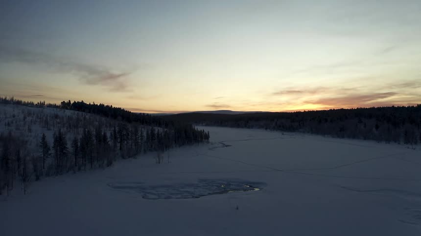 Sunset over frozen river between hills covered in pine trees