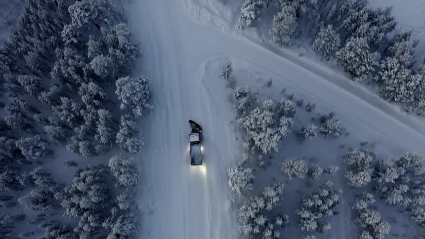 A snow plow passes through a fork in the road by a forest
