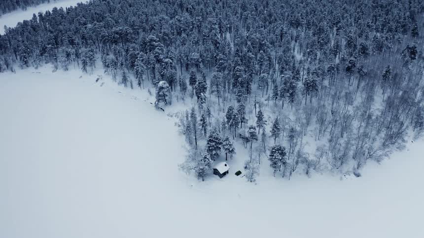 Aerial of a lone cabin in the woods surrounded by snow