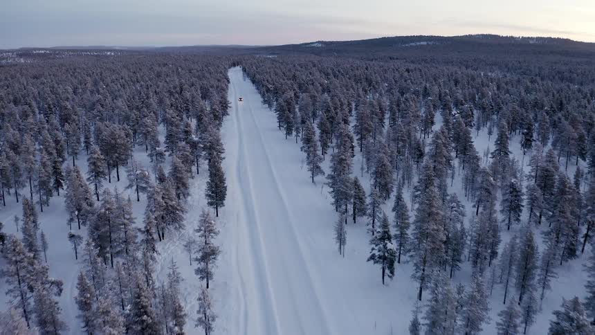 Aerial view of a road through a snowy forest with a truck on it