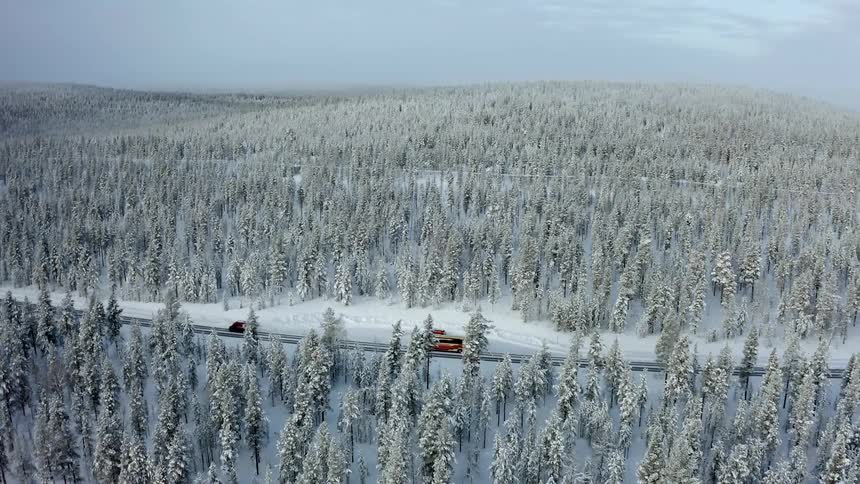 Vehicles drive down a road that winds through a snowy forest