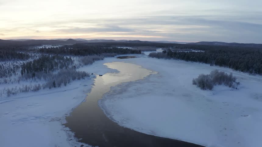 Bridge crosses partially frozen river surrounded by conifer forest