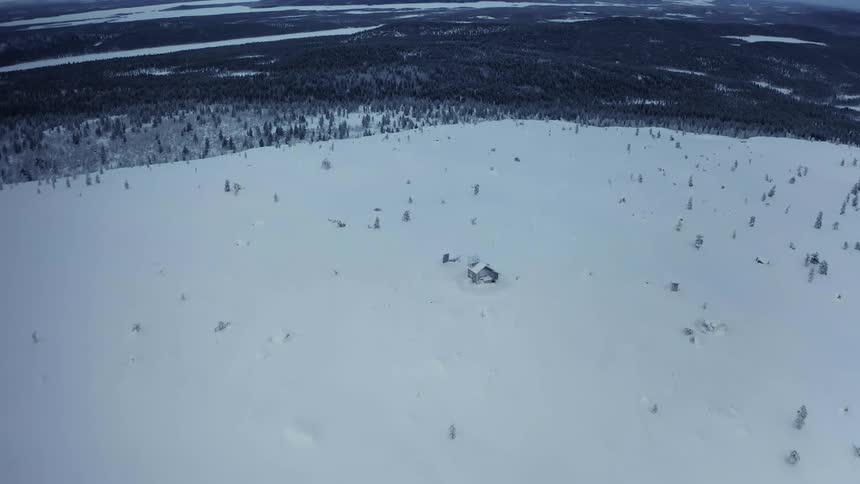 A small isolated cabin surrounded by snow with trees the sky and clouds in the background