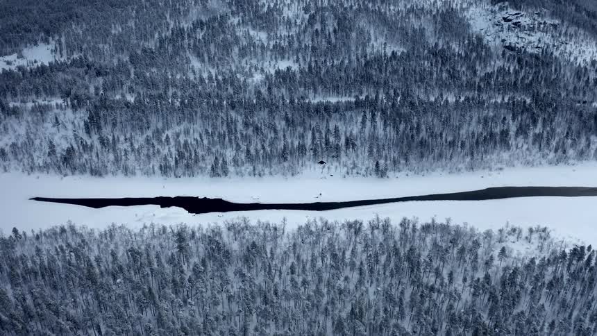 A snow covered river that runs through a forest starts to melt in the middle