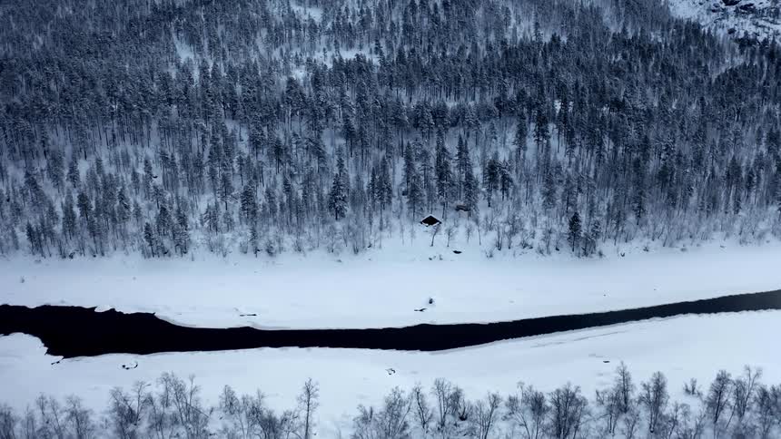Snow partially covers a river and the surrounding forest