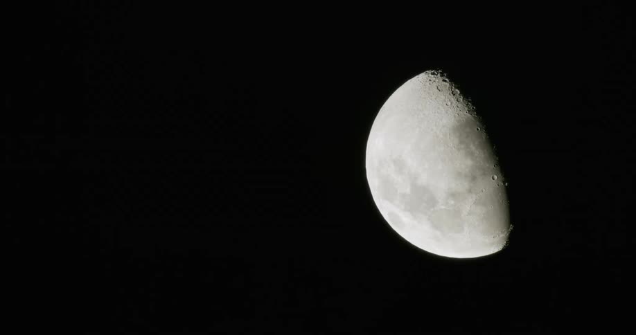 A partial moon stands against a pitch black night sky