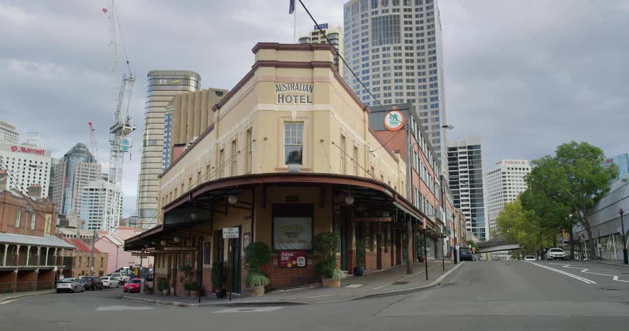 A hotel on a city street with cars parked on it and skyscrapers and construction cranes in the background