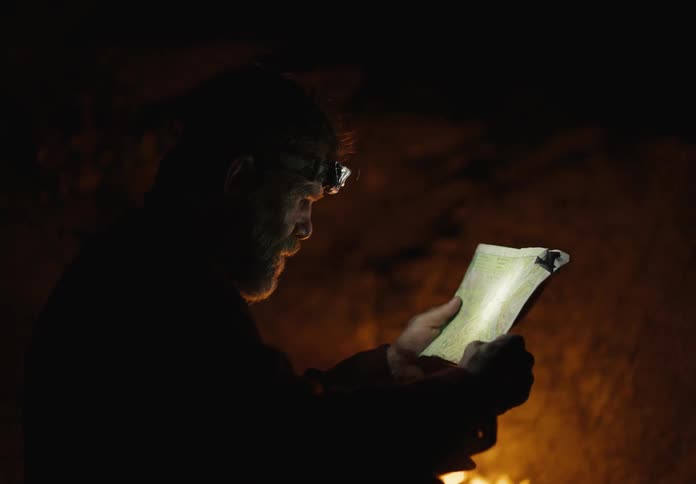 A man reads a map by the campfire