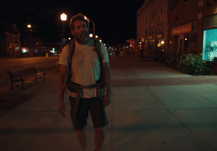 Middle aged man with a beard and wearing a backpack walks down the empty street at night