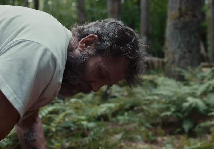 Man bends down to dig in forest near tree trunks and plants