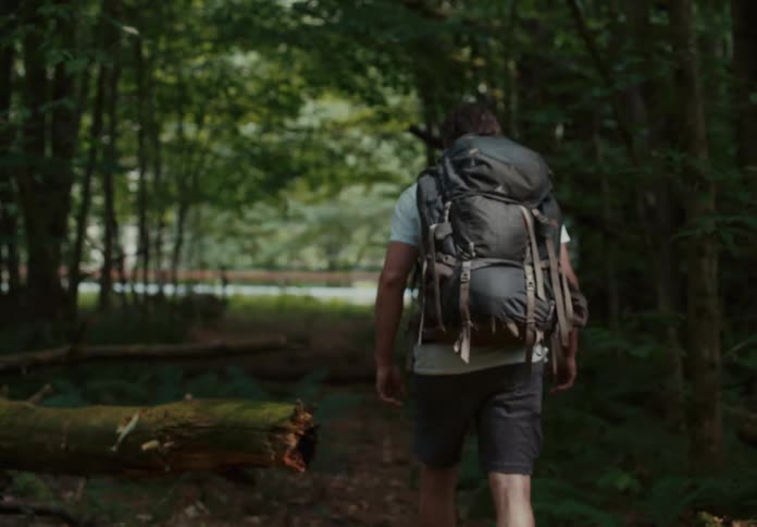Middle aged man with a beard and wearing a backpack walks up in the forest