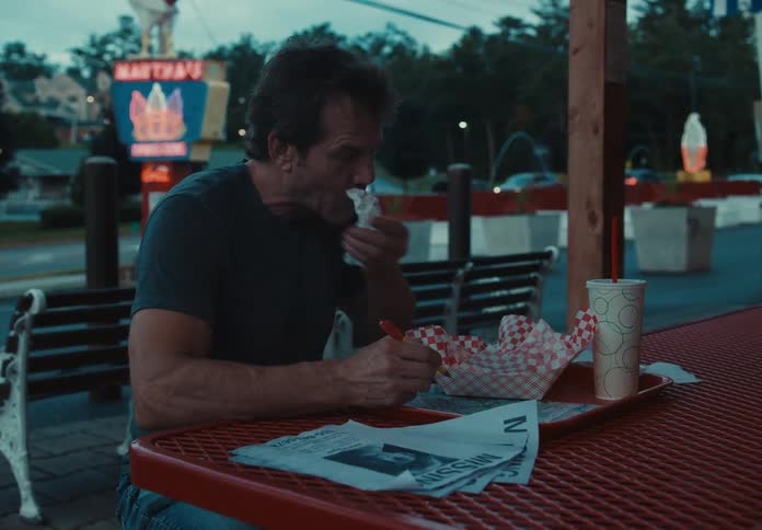 Man eats a hamburger outside a restaurant in the street of a small town