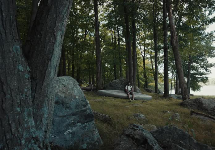 A man in a forest flips over a canoe and sits down on it