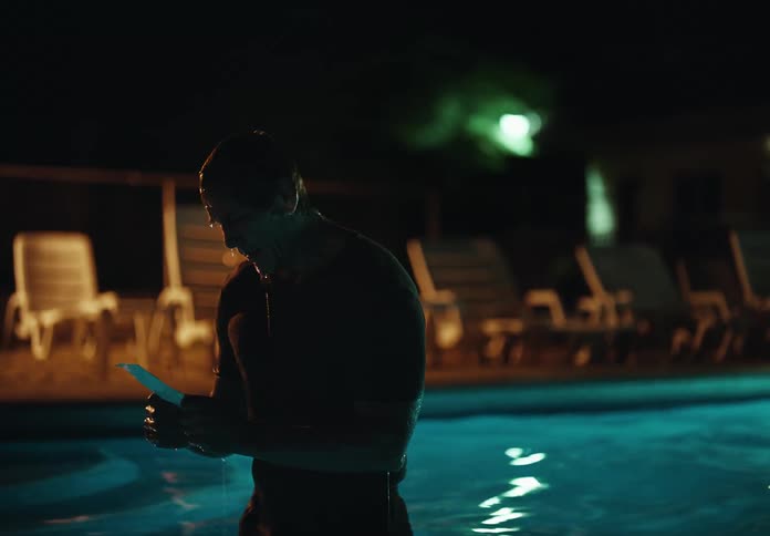 A man stands in a pool looking at something in his hands