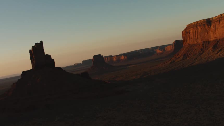 Sun tints clouds on horizon and casts shadows along ground among mesa