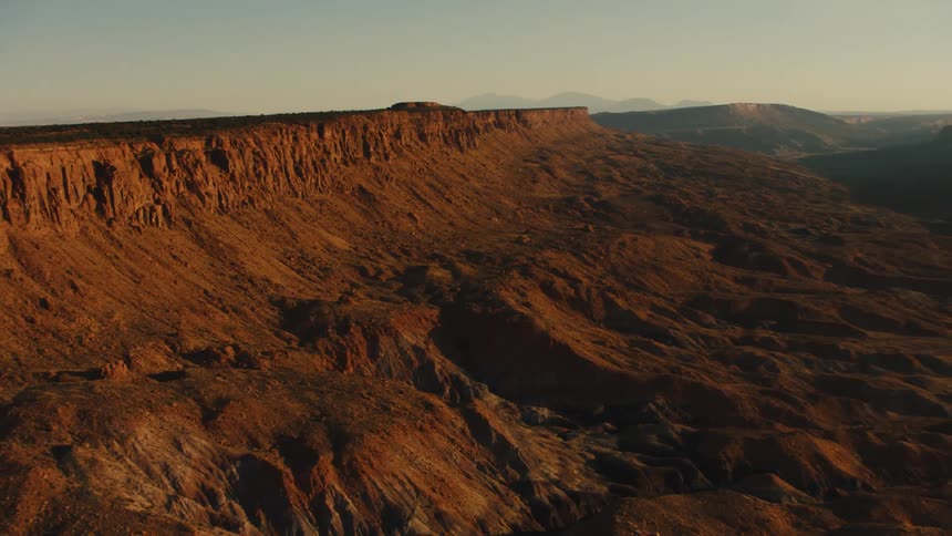 A desert with plateaus with the sky mountains and clouds in the background