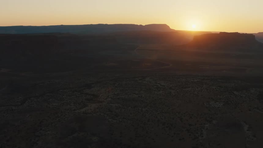 Sun sits on horizon turning sky red and shining past plateau and mountains onto scrub dotted land