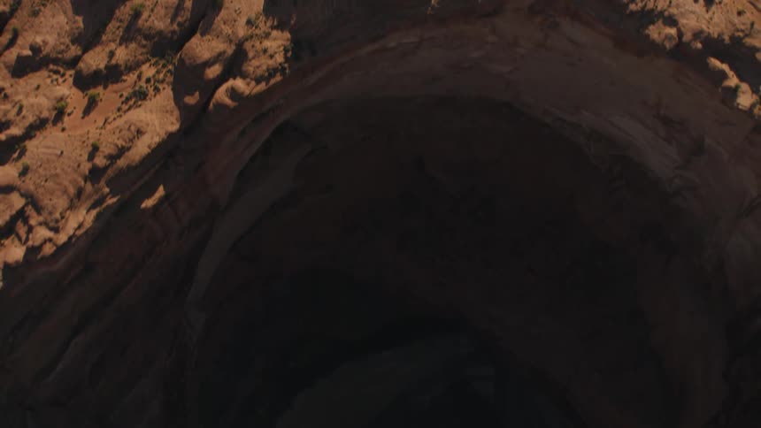 A cave sits at the base of a vast canyon