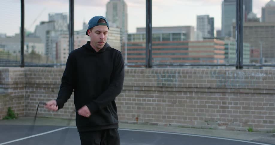Man with a black hoodie and a cap jumps rope on the rooftop of a building
