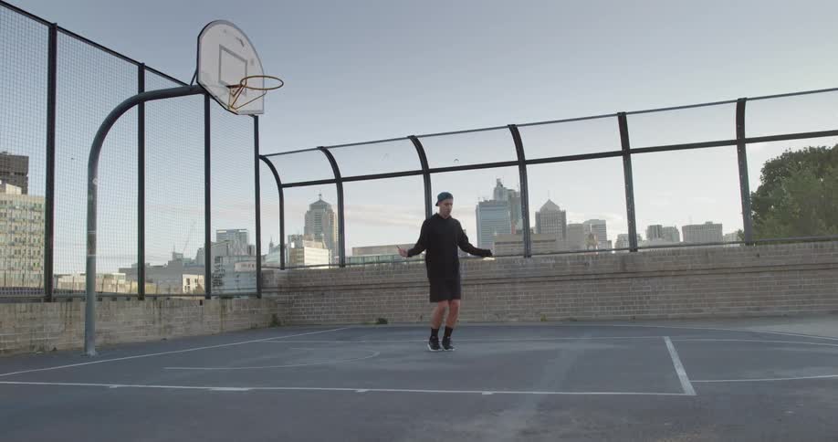 A man on a basketball court jumping rope with the city skyline in the background