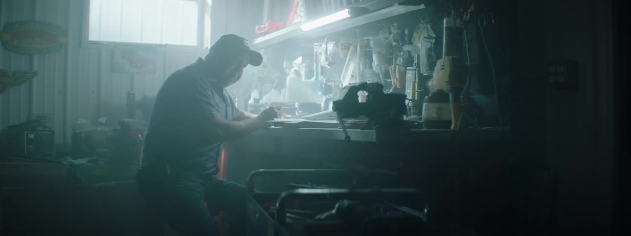 A man sits down at a bench writing something in the dark