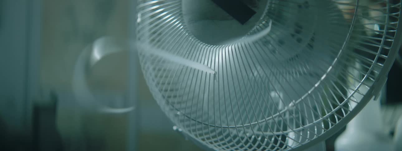 Desk fan spinning in a dimly lit room
