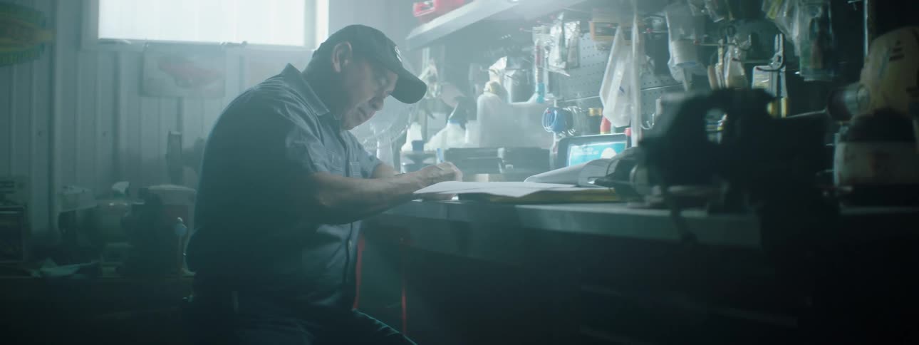 A mechanic sits at a bench and writes