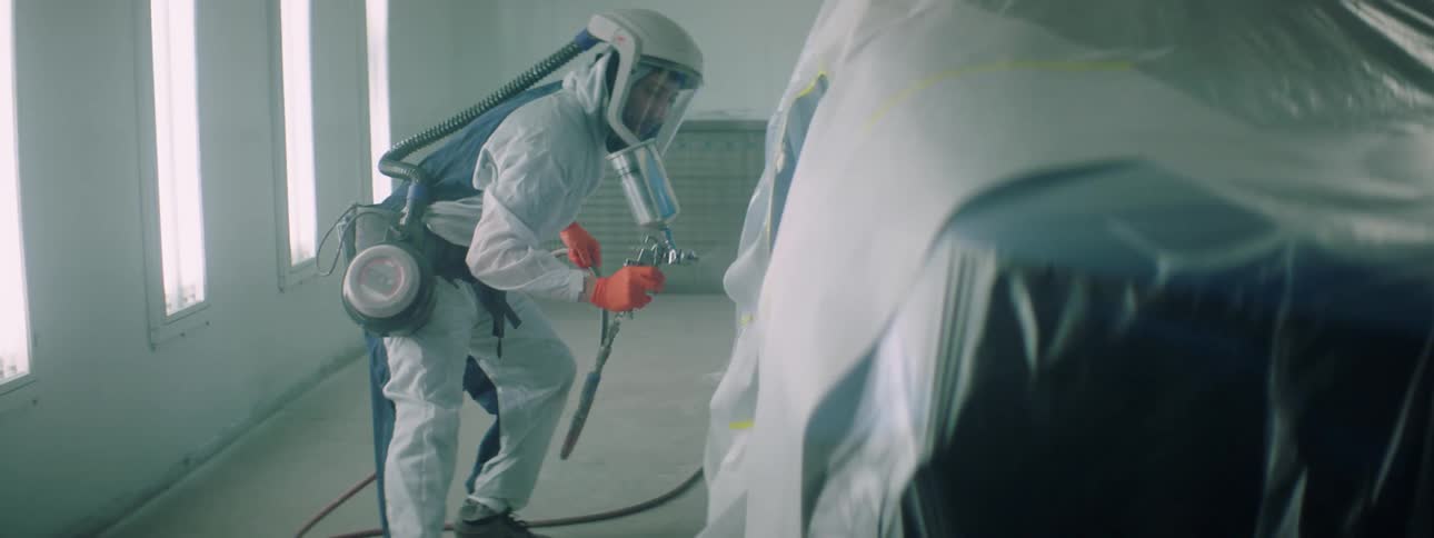 A man wears a hazmat suit as he spray paints a pickup truck