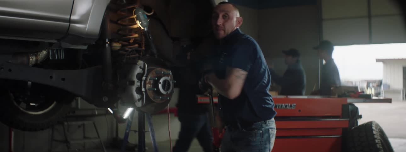 A mechanic uses a wrench to remove vehicle part and stops to pose with the tool