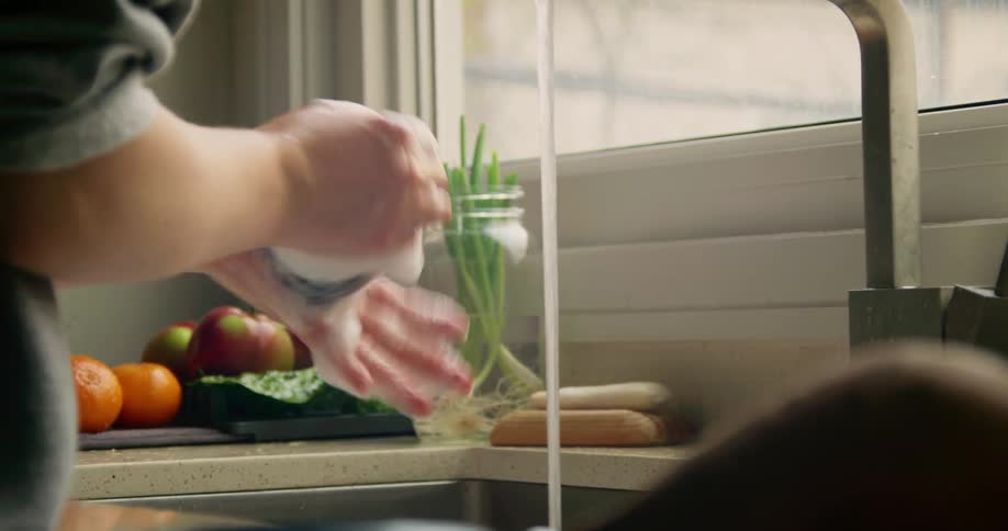 Person washing and rinsing produce at the kitchen sink