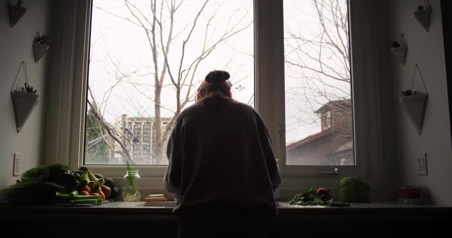 Woman prepares vegetables in sink near window showing leafless trees