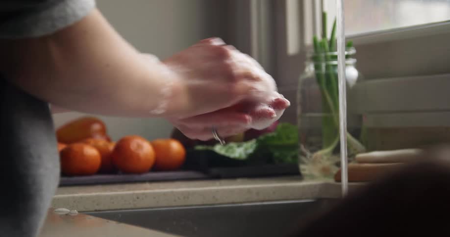A woman washes an orange at the kitchen sink rolling it and scrubbing with suds