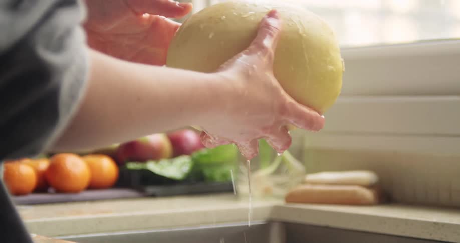 Person wearing sweatshirt rinses squash and places it with other produce to the side of sink