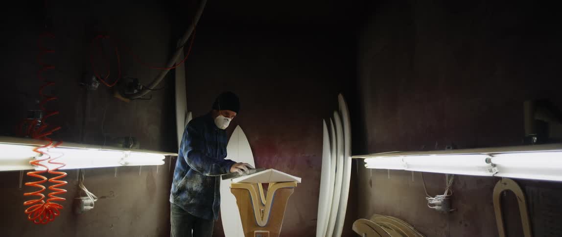 A man polishes a surfboard in a shop