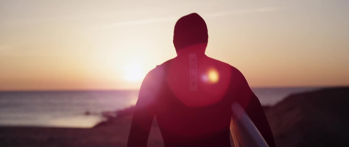 A man walks across an empty beach holding a surfboard