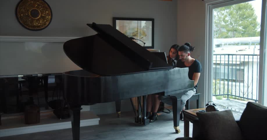 A man and woman sit at a piano together and play