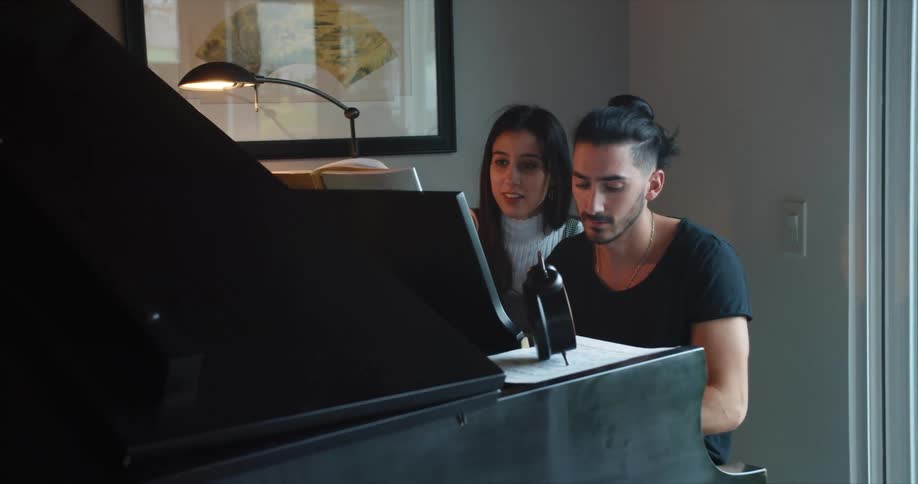 A man and woman sit together playing a piano