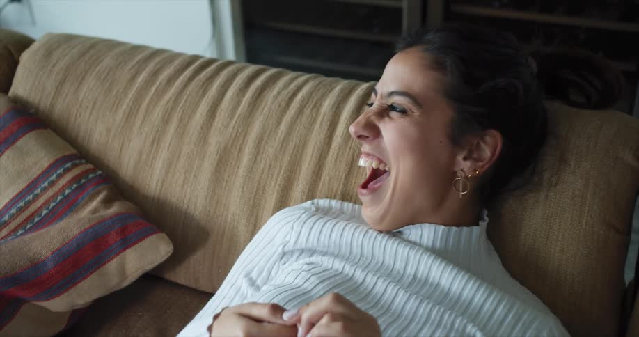 A woman sits on the couch and laughs at someone else in the room