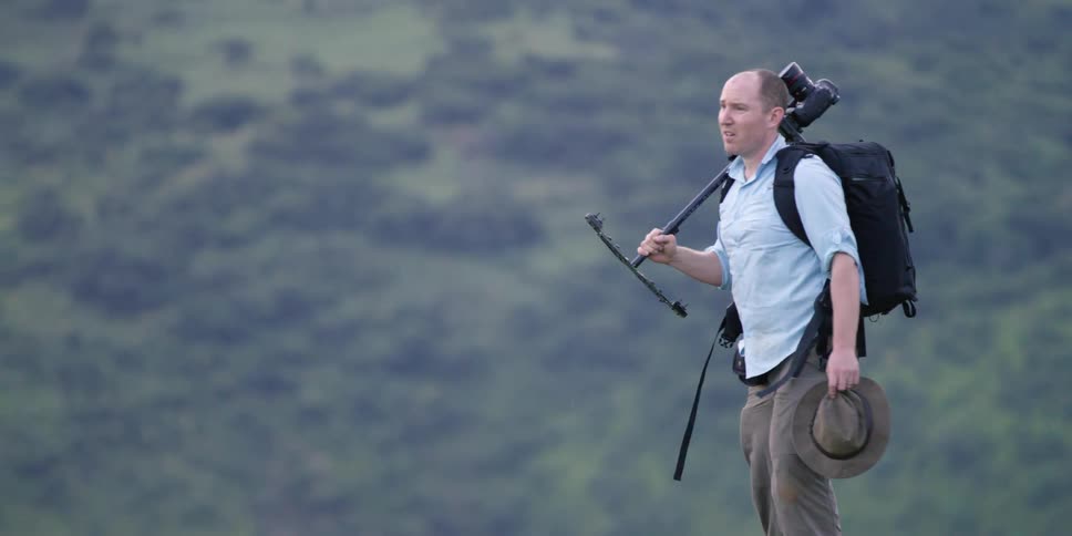A man is carrying a camera on a tripod as he hikes