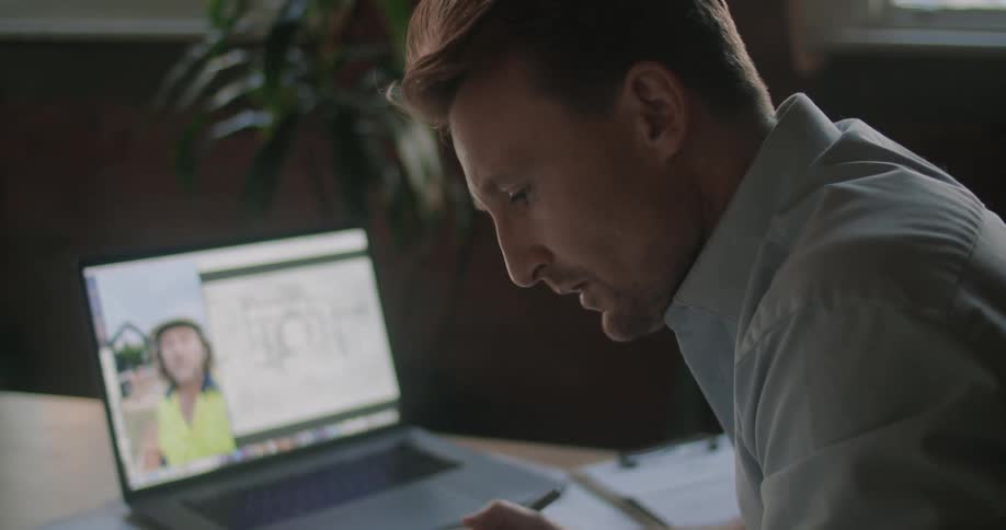 A man looks over blueprints while talking to someone on the laptop