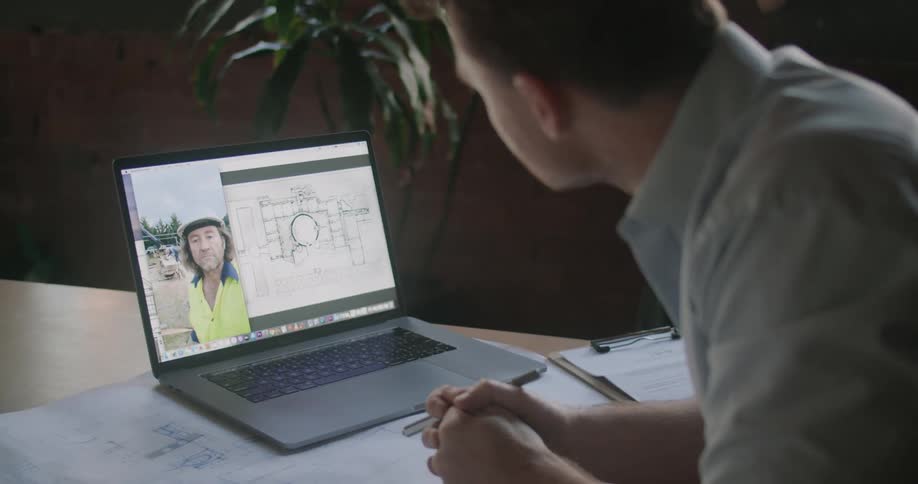 A man in an office talks with someone on the laptop