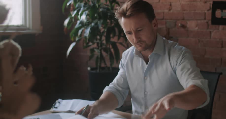 A man sits at a desk with blue prints spread out and under his laptop while he works