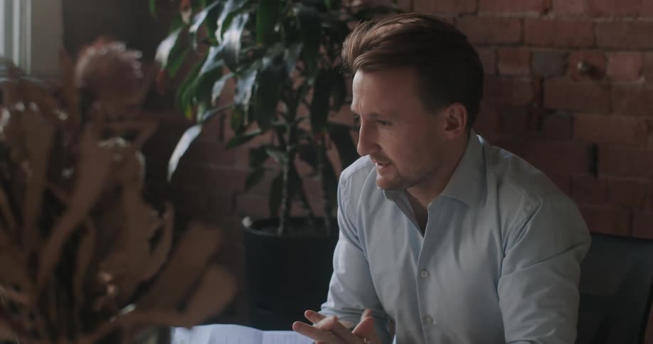 A man is talking at his desk