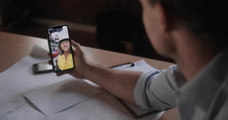 A man sitting at a table having a video chat on his smartphone with another man
