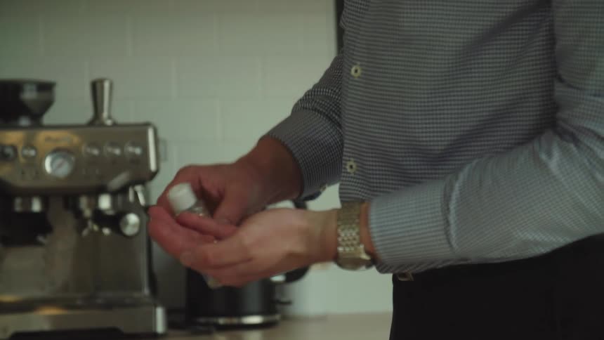 A man picks up a bottle of hand sanitizer from the kitchen counter and applies some to his hands