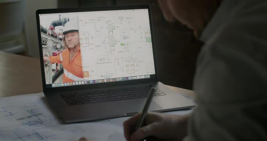 A man sits at a table with a laptop watching a video or stream of a man describing something