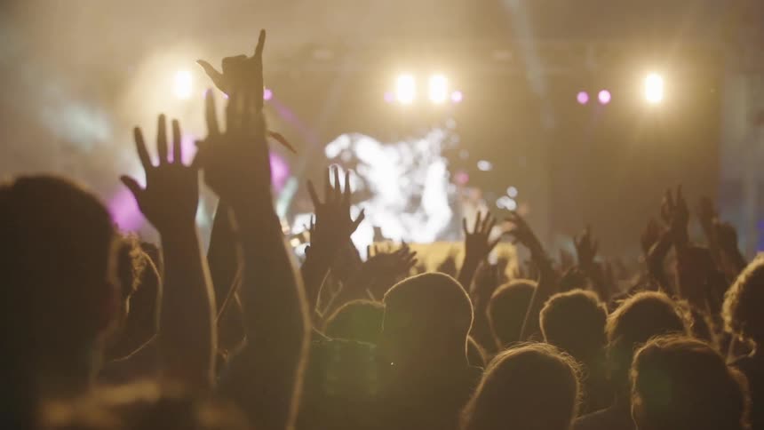 People at a concert with their hands in the air with people on stage with a big screen behind them