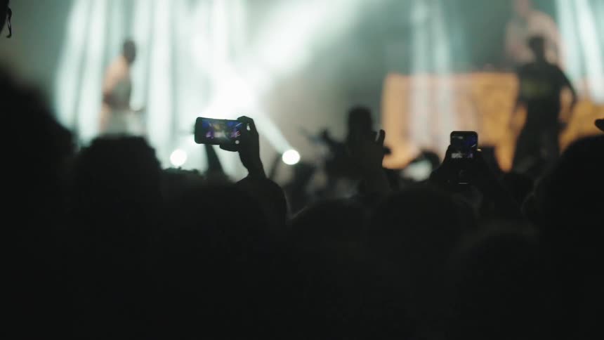 Crowd in a concert cheers while musicians perform in the stage