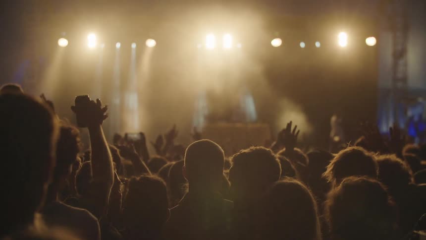 The audience with hands raised in the air as the lights on stage flash and shine